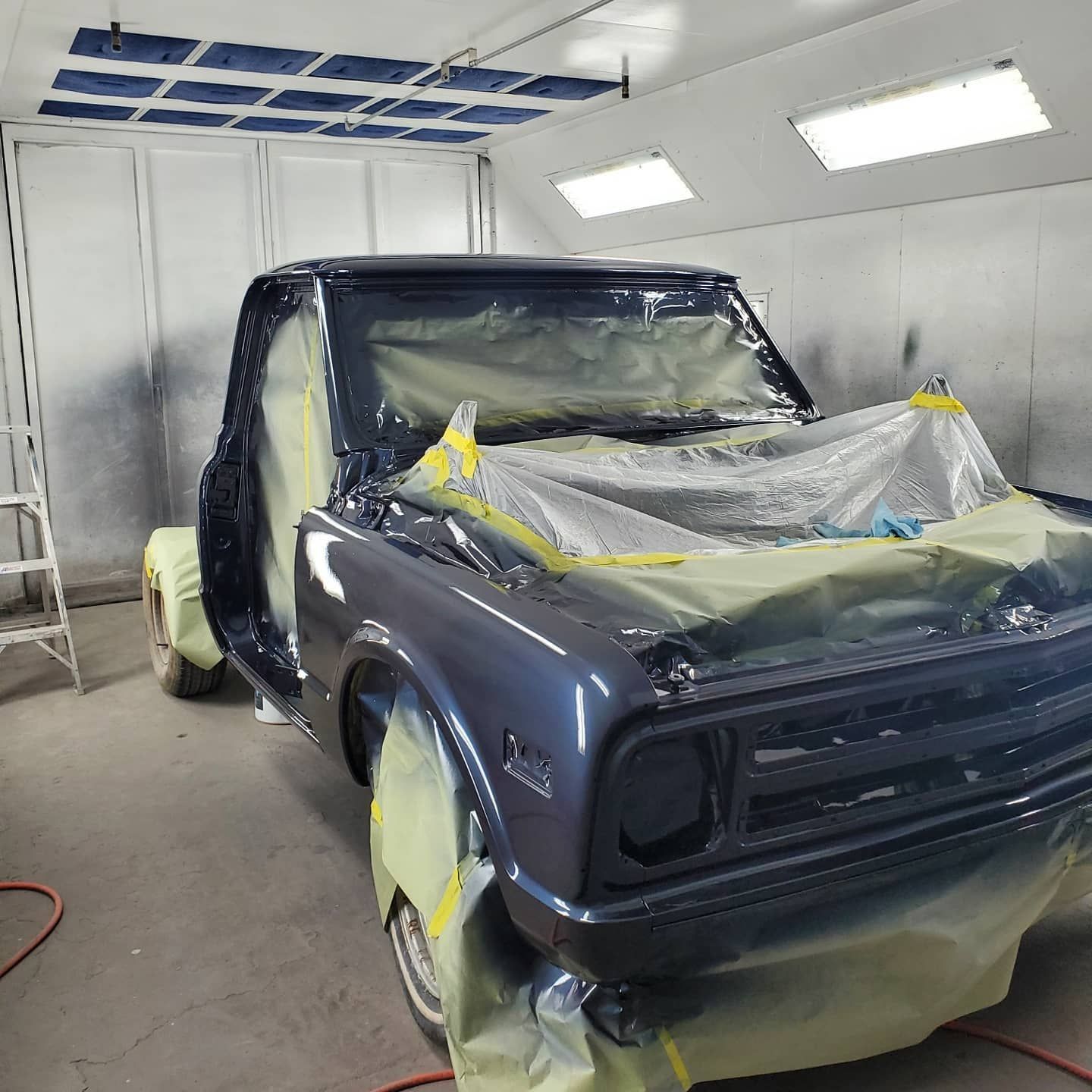Classic gray pickup truck in a paint booth, masked for painting.