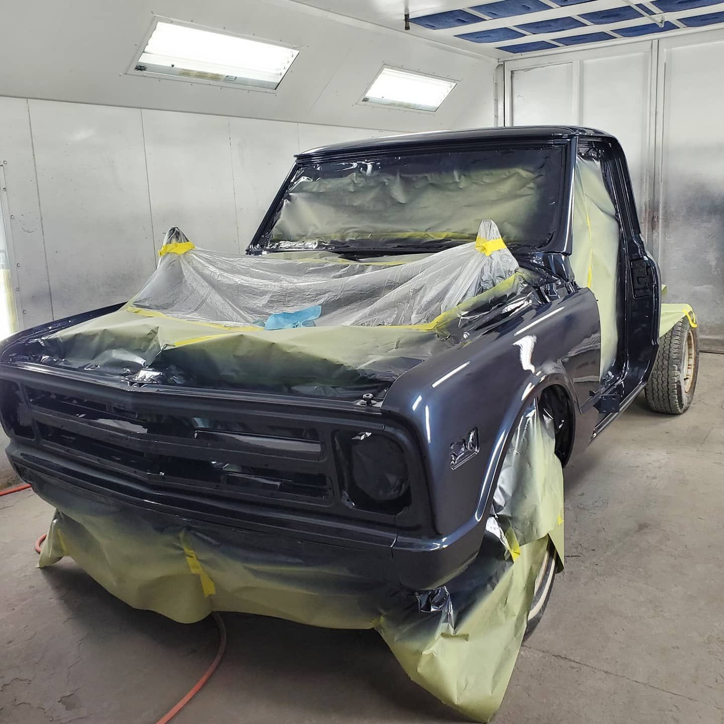 Classic blue Chevy pickup truck in a paint booth, masked for painting.