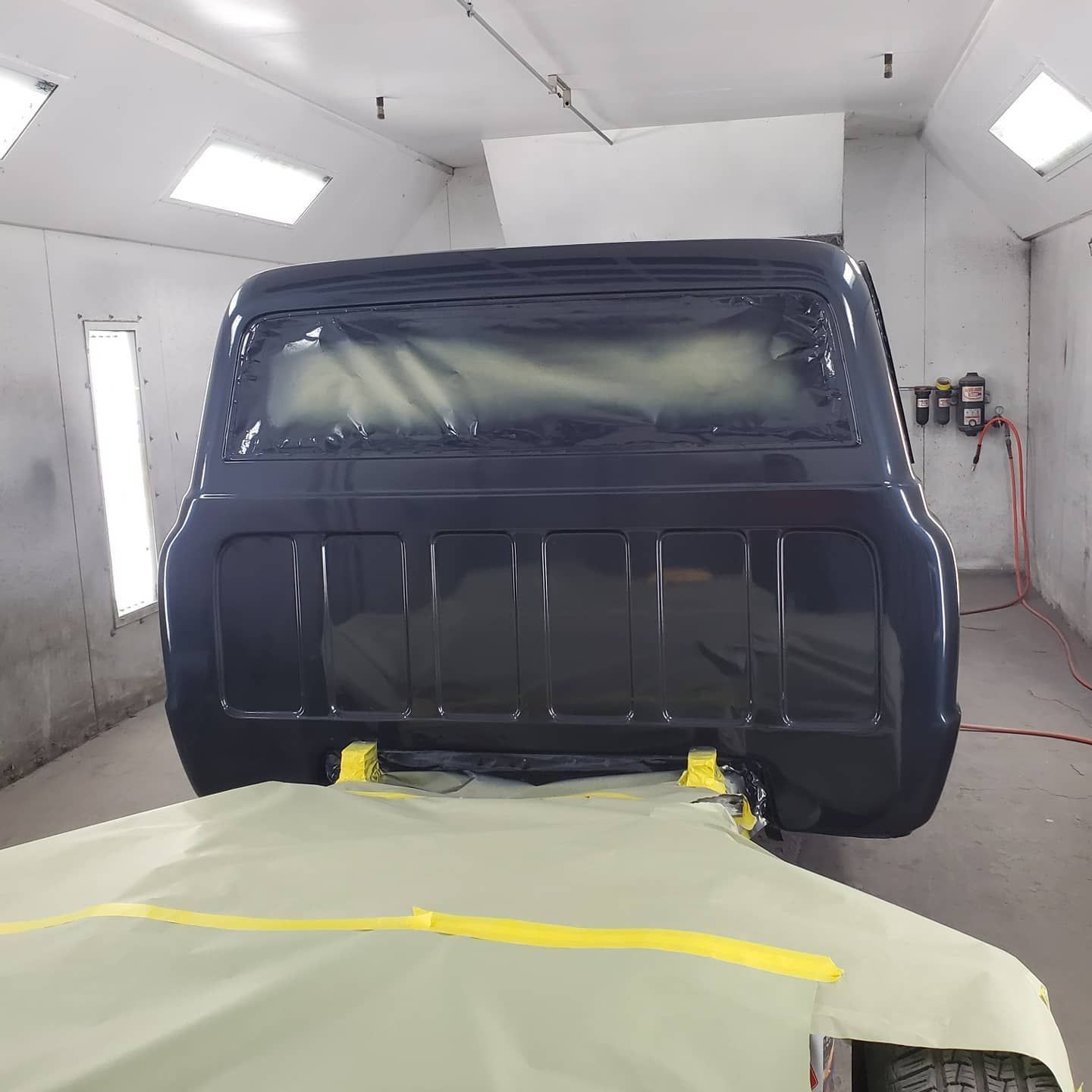 Dark blue truck cab in a paint booth, partially masked and painted.