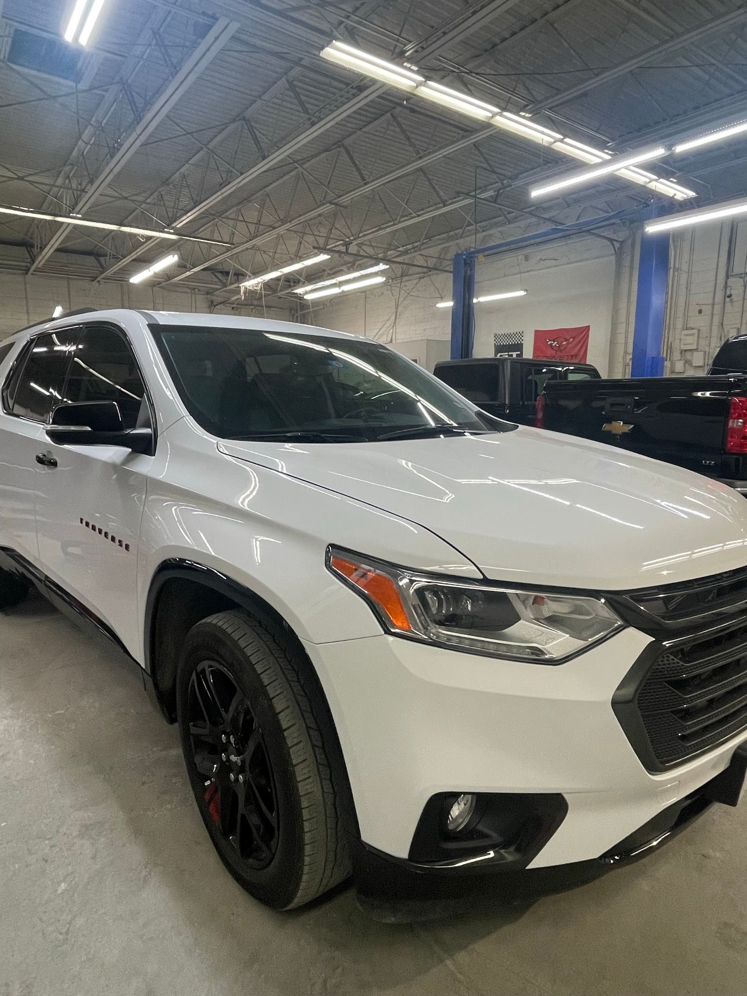 White Chevrolet Traverse SUV parked inside a garage. Black wheels and accents, lit by overhead lights.