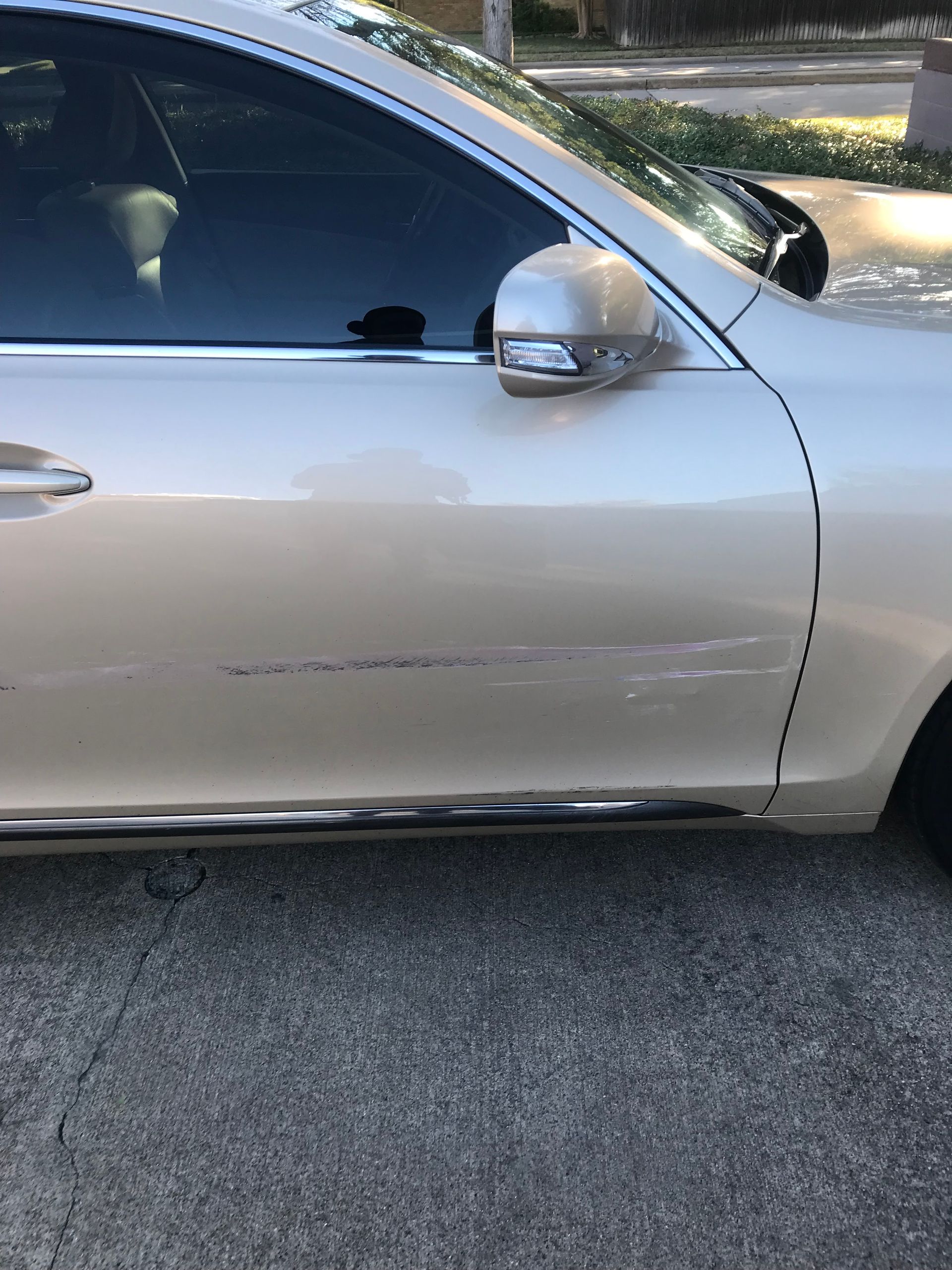 Gold car with scratches on the door, parked on a driveway.
