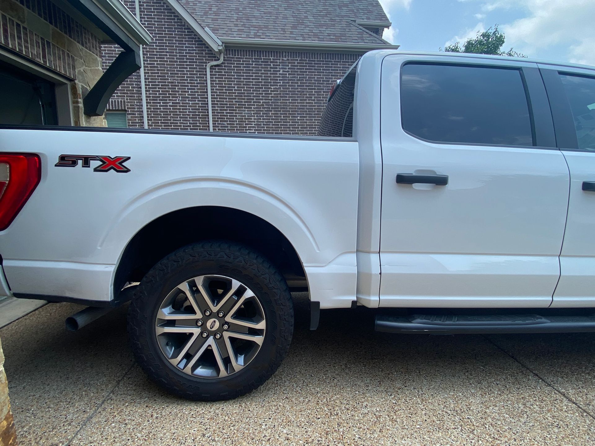 White Ford F-150 STX pickup truck parked on a paved driveway in front of a brick building.