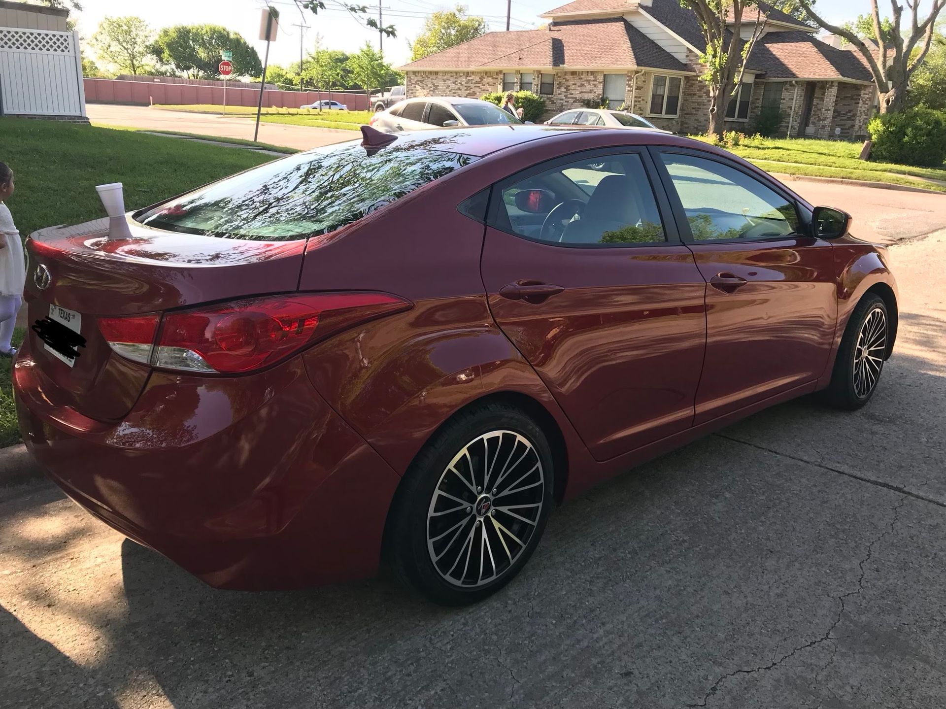 Red Hyundai Elantra parked on a driveway. Black and silver rims. Houses and street in the background.