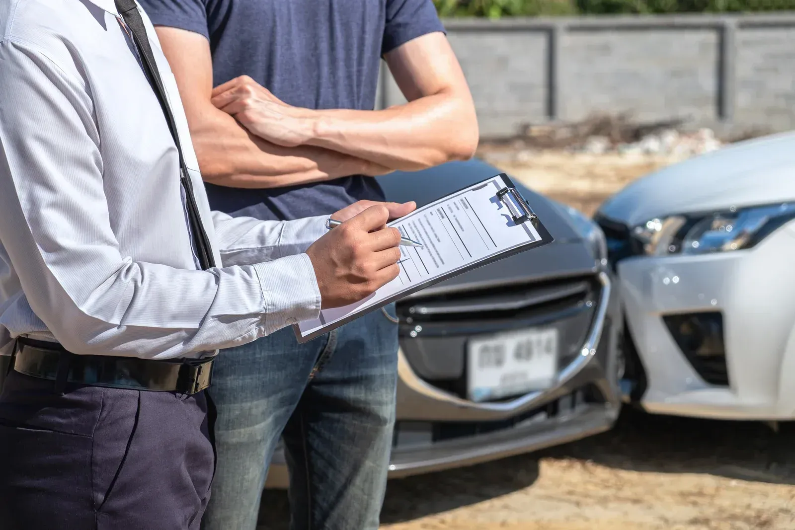 Two men examining a document near damaged cars after an accident.