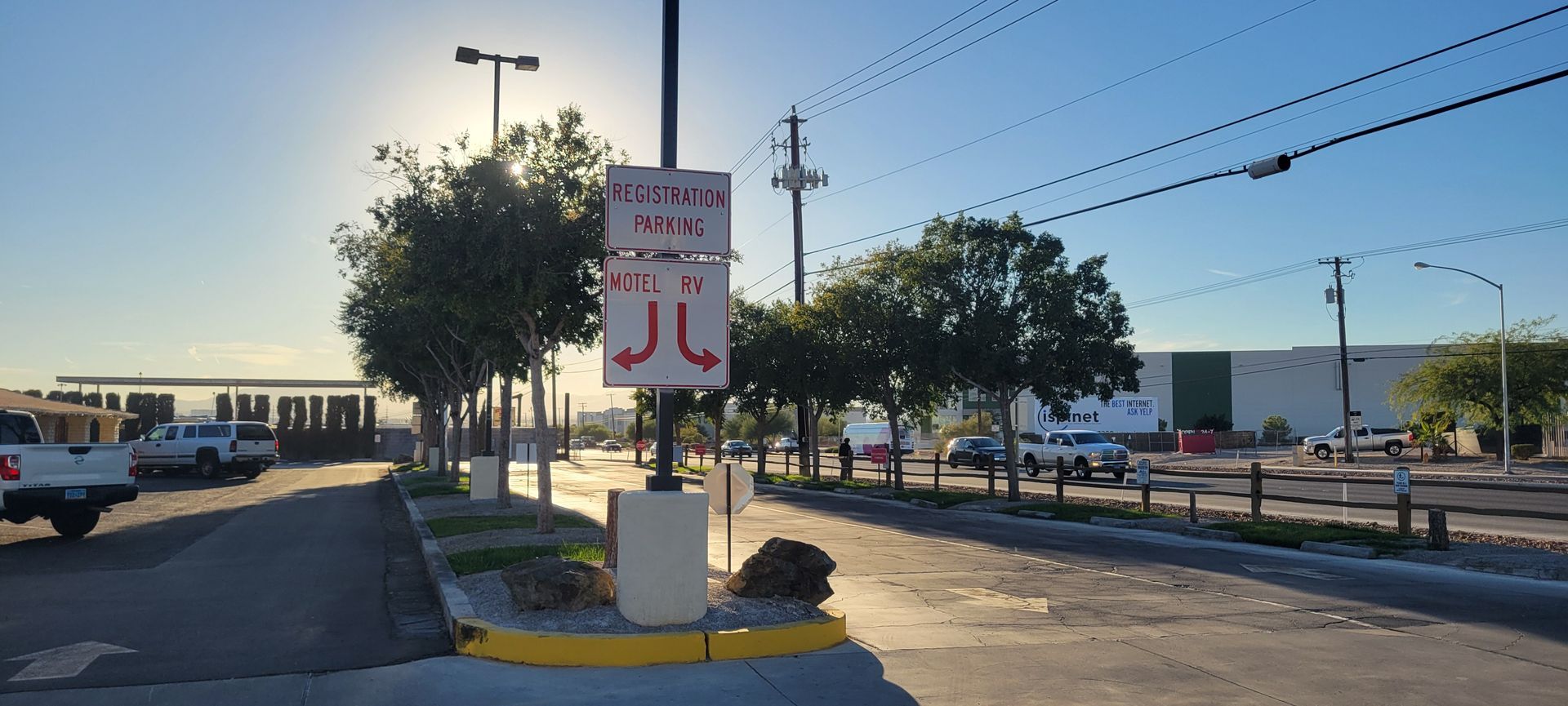 A street scene with a signpost, trees, buildings, and a bright sky with sun.