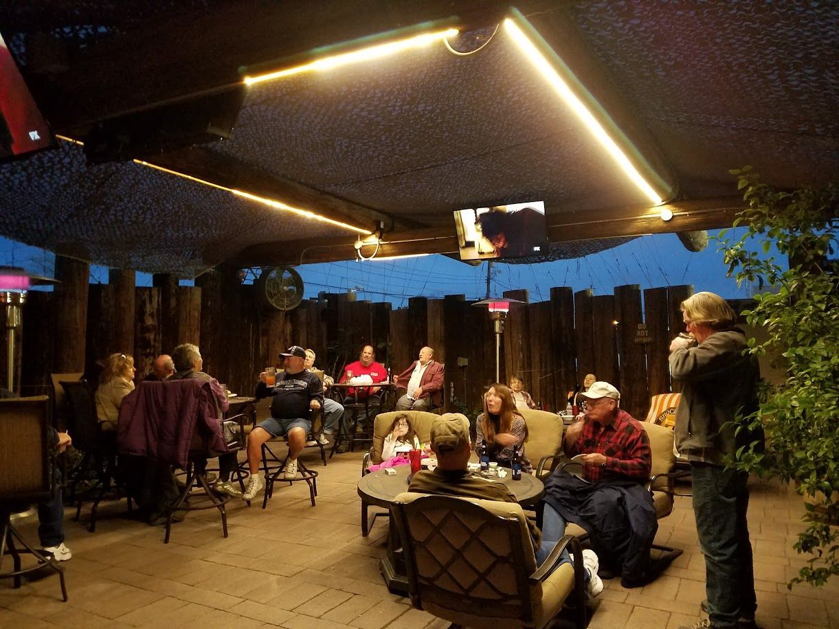 Outdoor patio with people seated at tables, under a canopy with string lights.