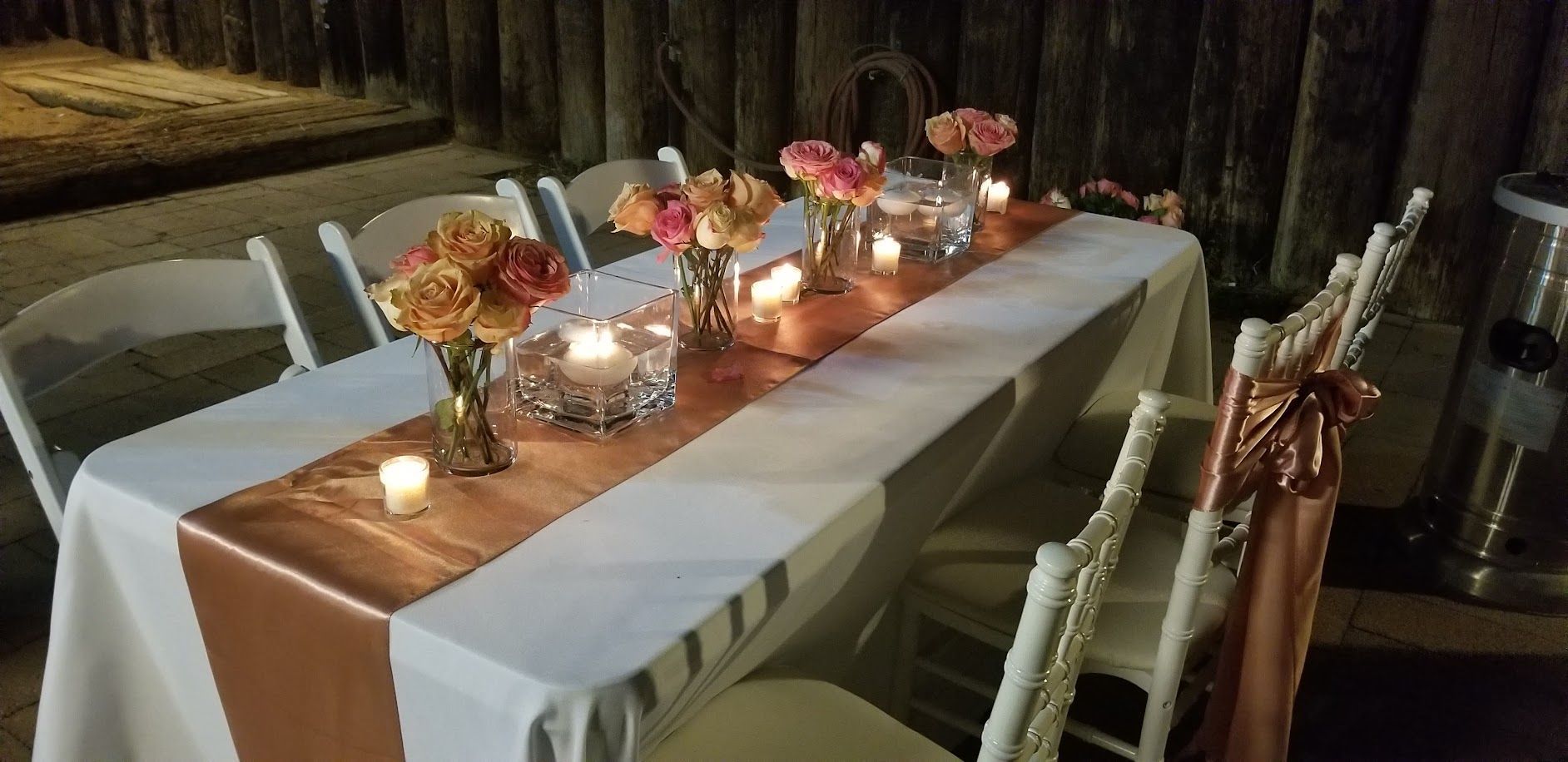 A long banquet table set for a celebration. It has flowers, candles, and a copper table runner.