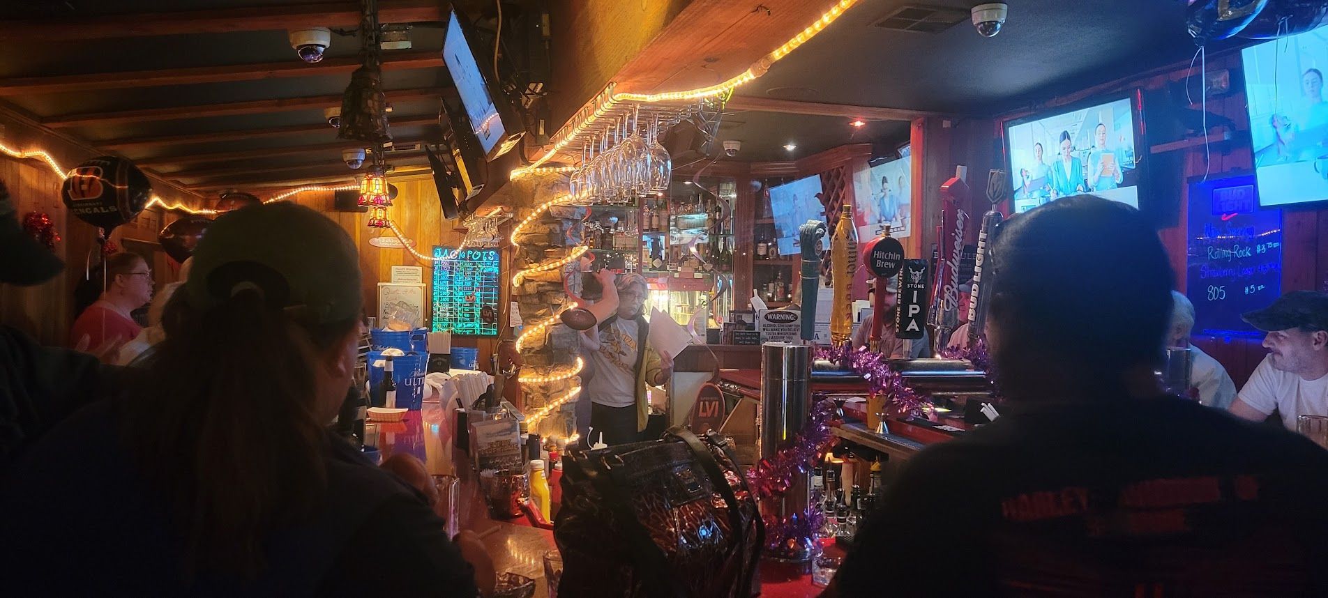 A bar with patrons; warm lighting, bottles and glasses, and TVs.