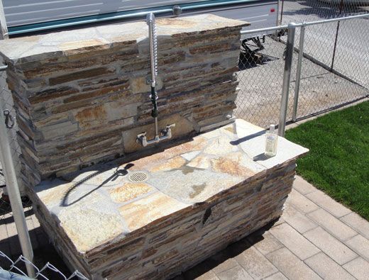 Outdoor stone sink with faucet and soap dispenser near a fence.