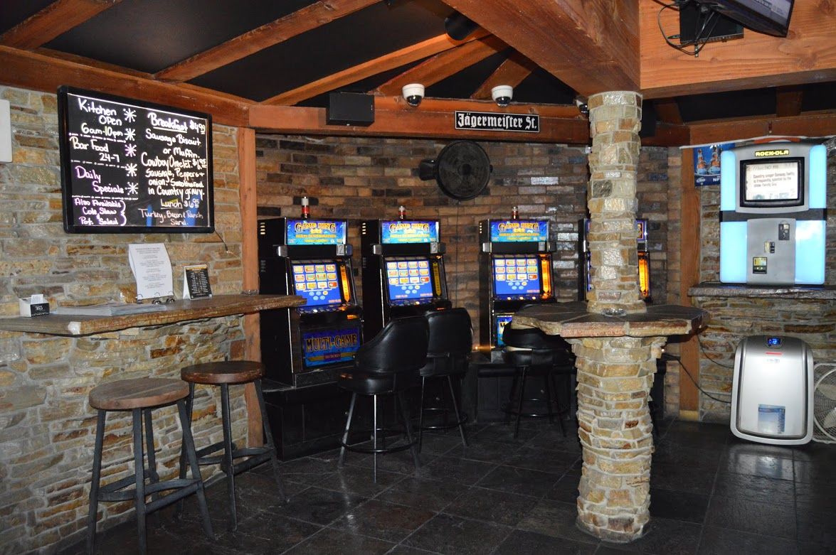 A dimly lit bar area with stone walls, wooden beams, slot machines, and bar stools.