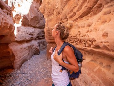 Woman with backpack exploring a narrow, sandstone canyon.