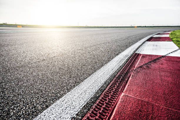 Race track with white and red curbing along edge, bright sunlight.