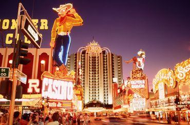 Neon cowboy sign on Fremont Street in Las Vegas, with casinos and street scene at dusk.