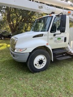 A white truck with a crane on top of it is parked in the grass.