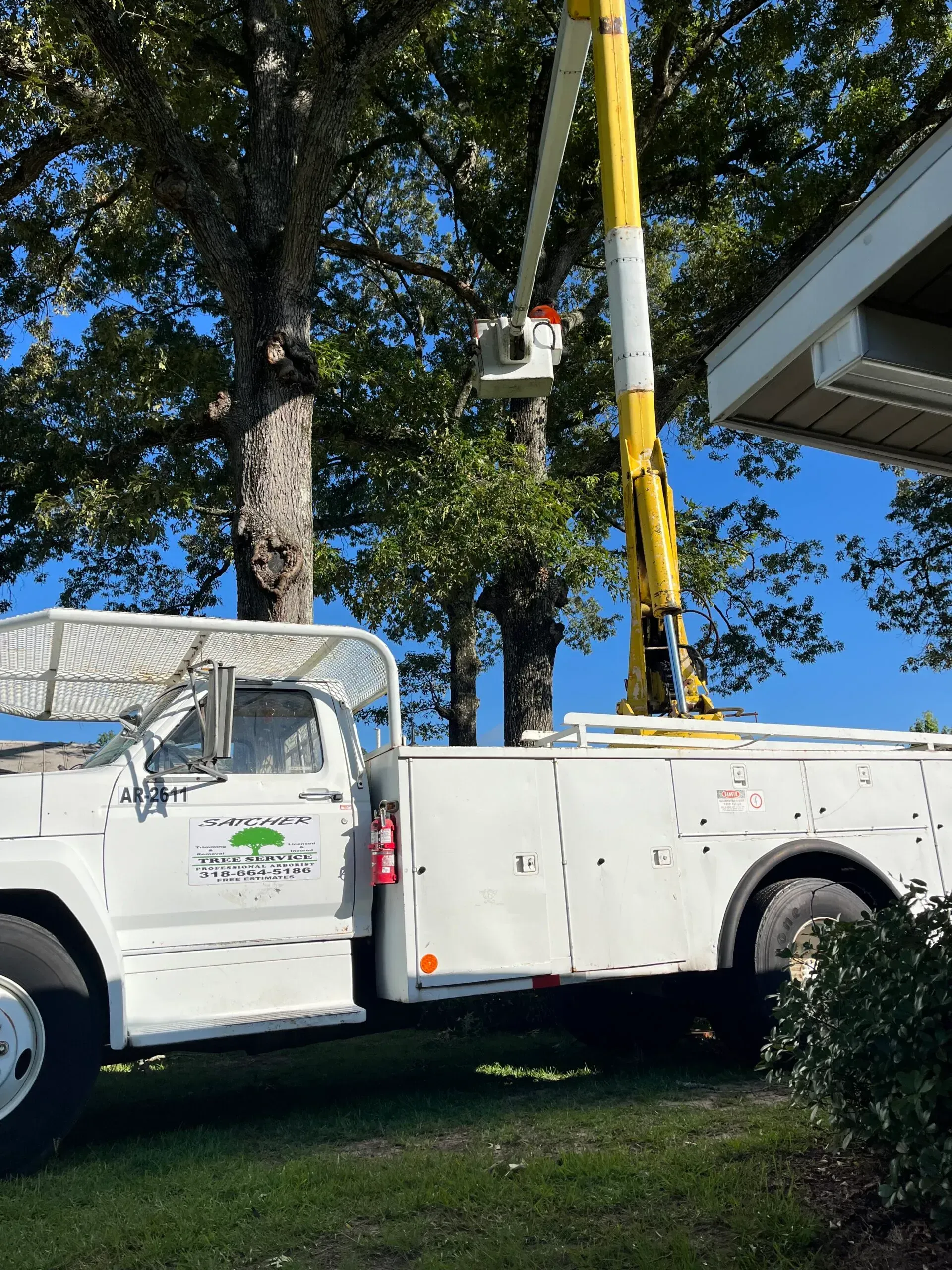 A white truck with a yellow crane on the back is parked in front of a house.