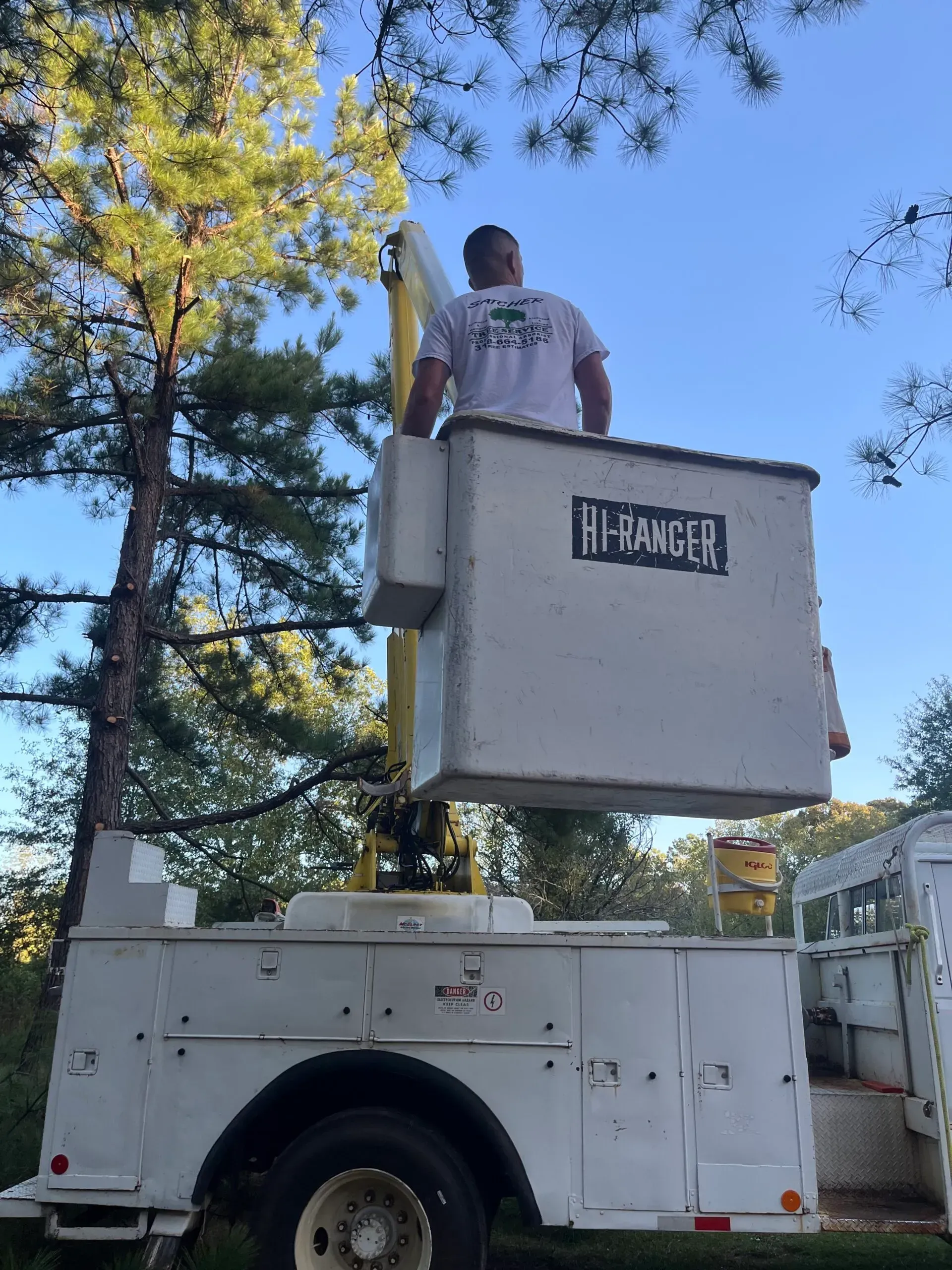 A man is standing in a bucket on top of a utility truck.