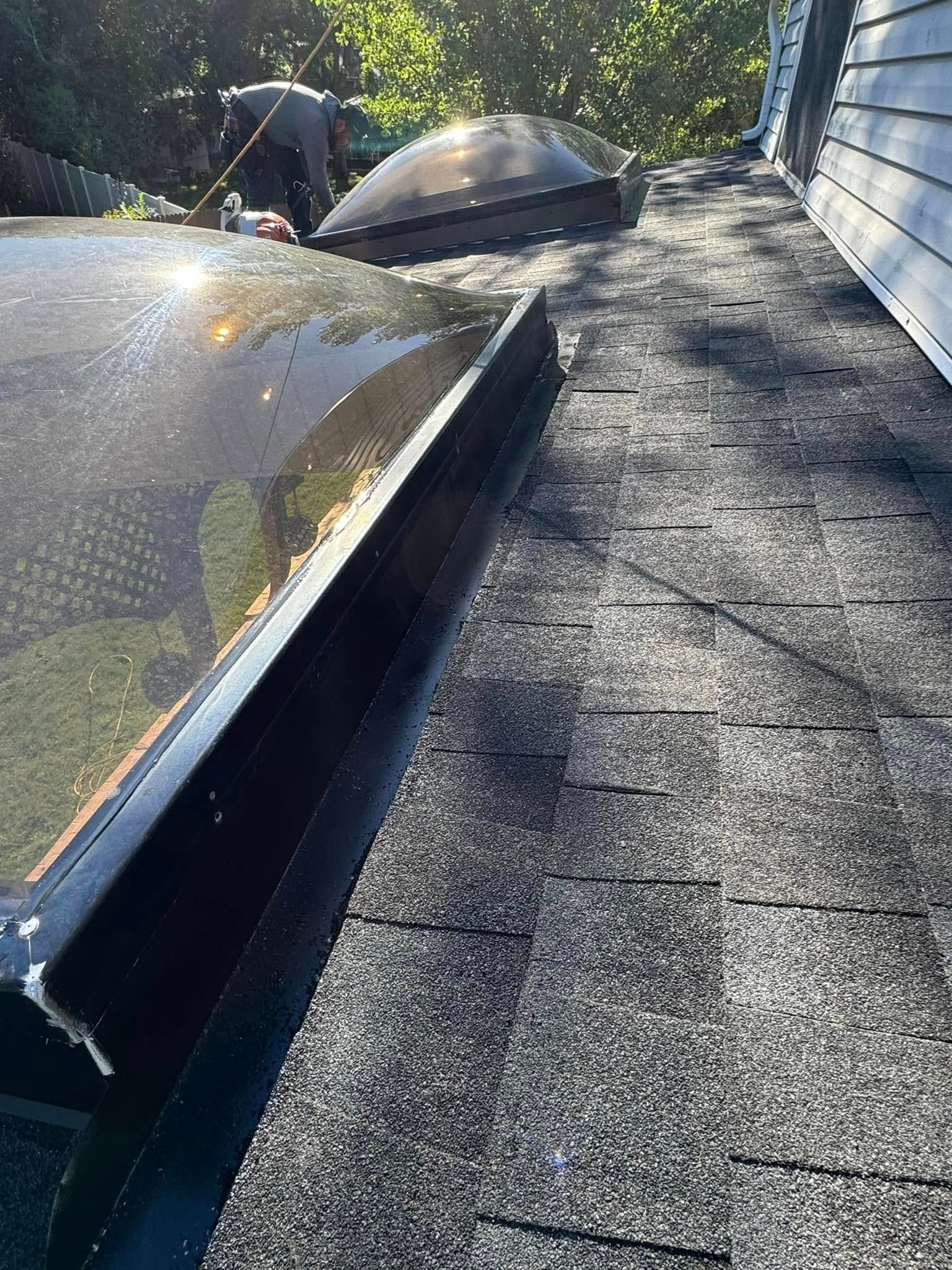 Black skylight on asphalt shingle roof. Sunlight reflects on its surface.