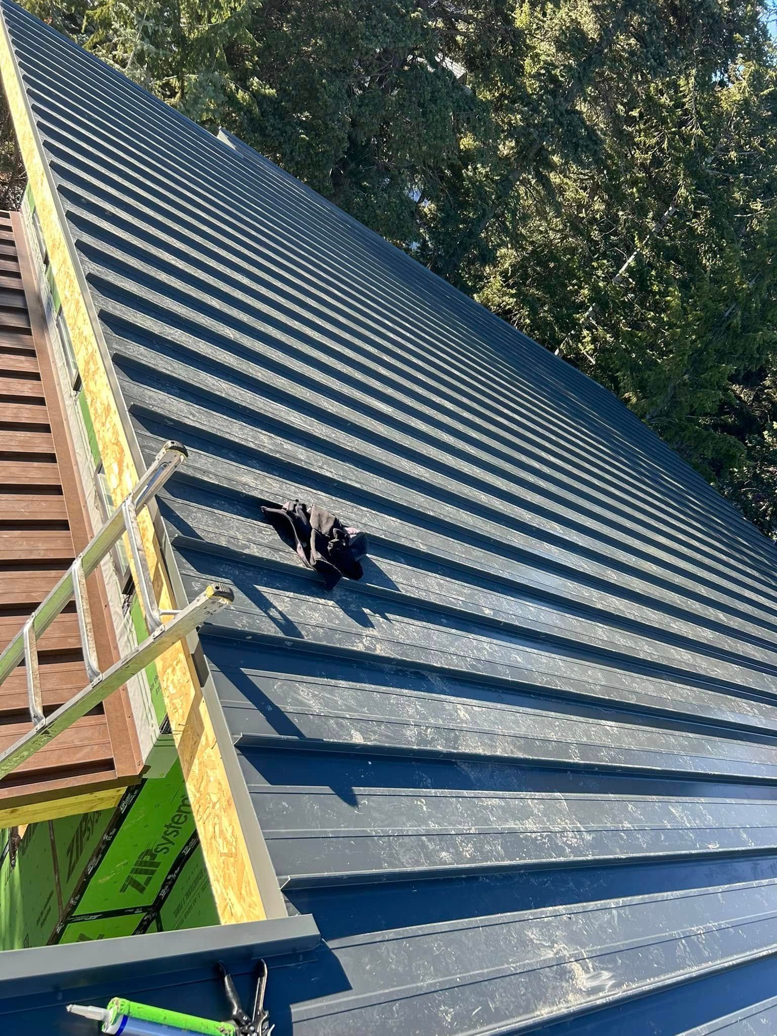 Metal roof being installed, dark gray color, with lumber framing and green sheathing visible.