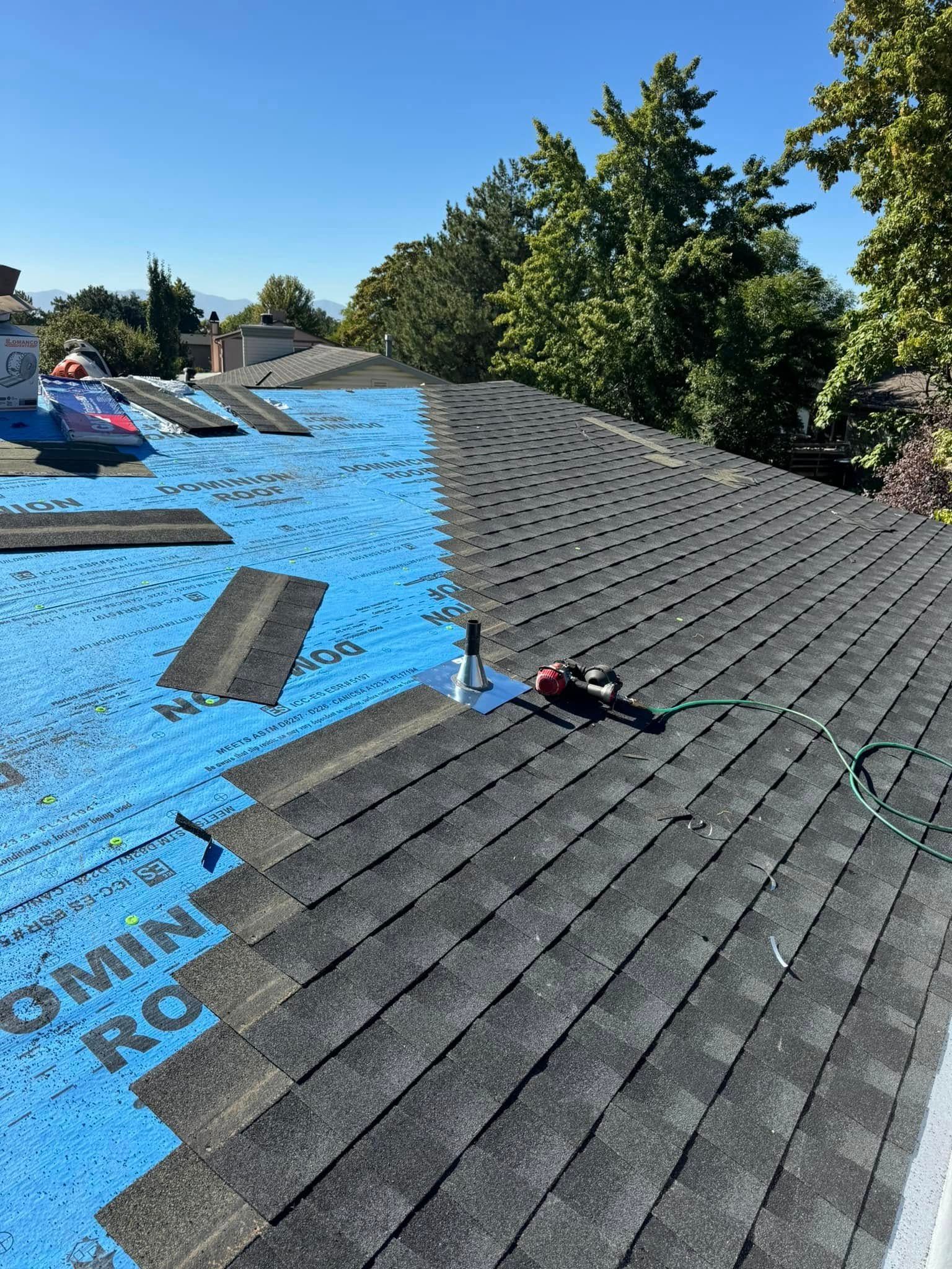 Roofing work in progress: blue underlayment, gray shingles, bright sunny day.