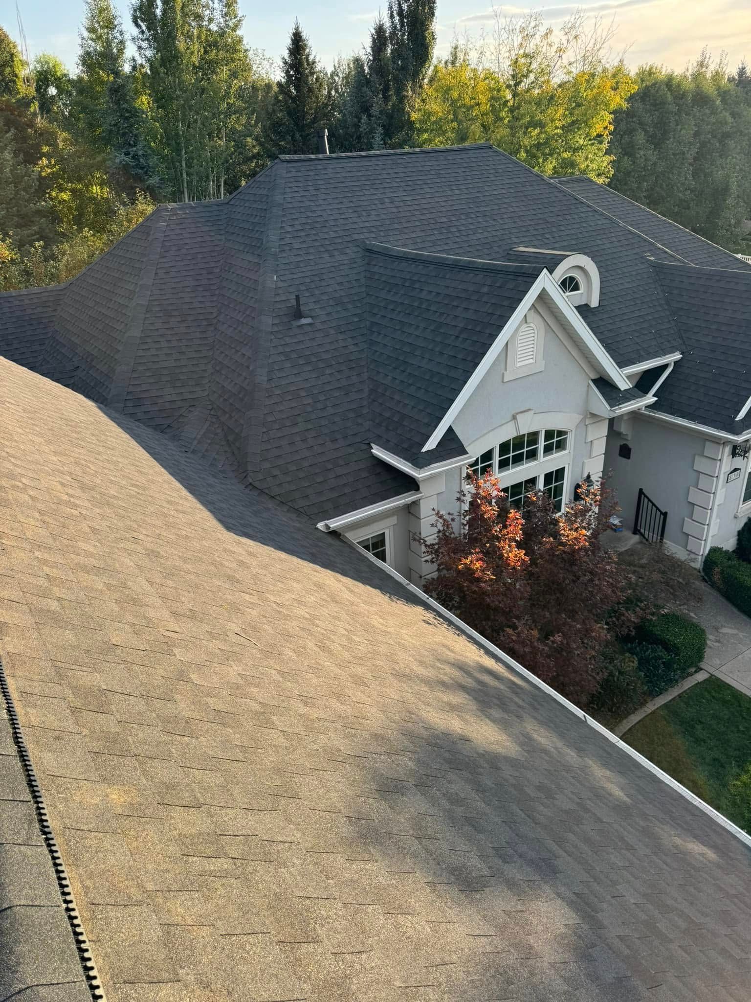 Overhead view of two roofs, one gray and one brown, with a light-colored house in the background.