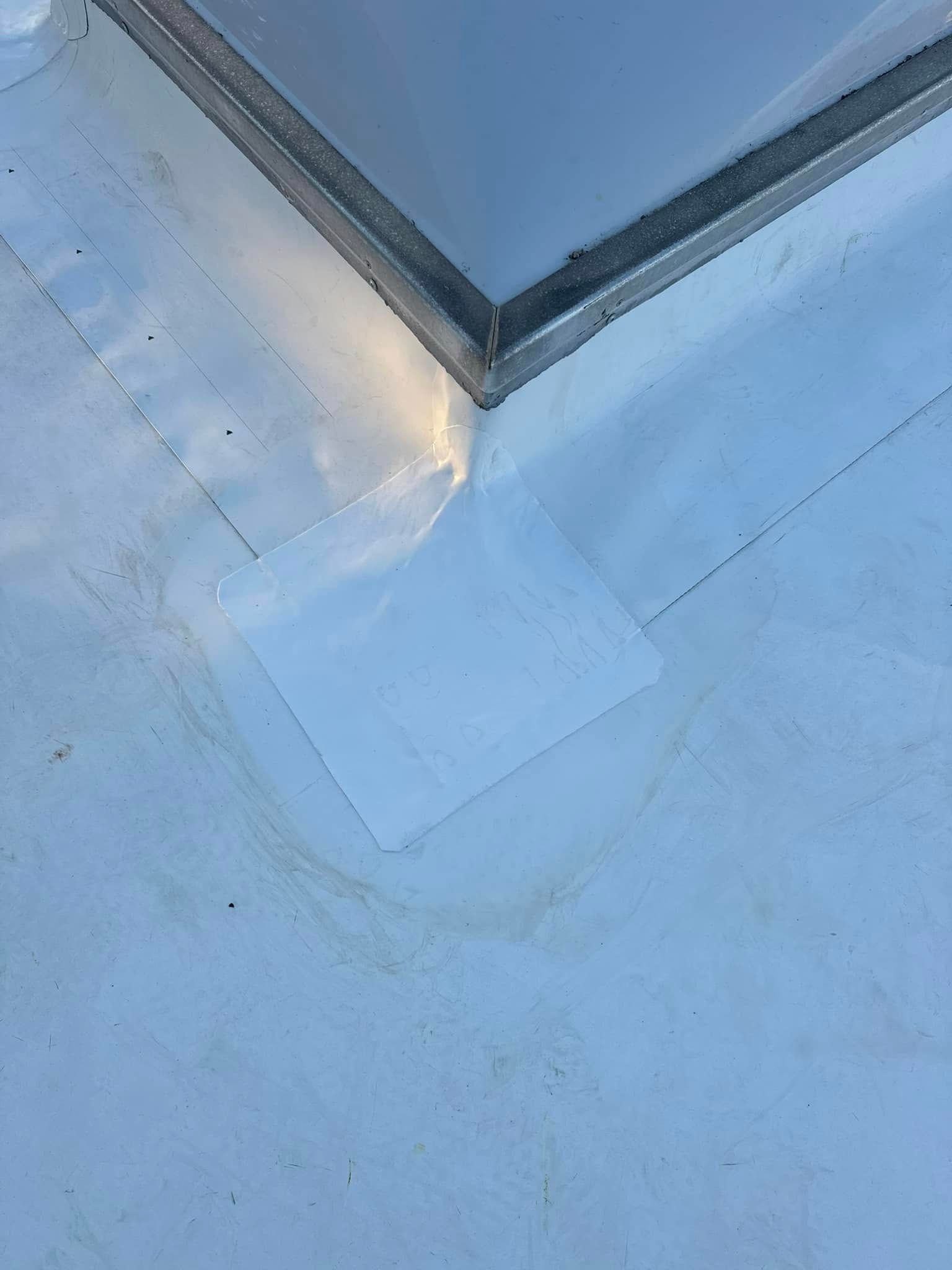 White roof with a square patch near a metal-framed skylight. Brown stains are visible on the roof.