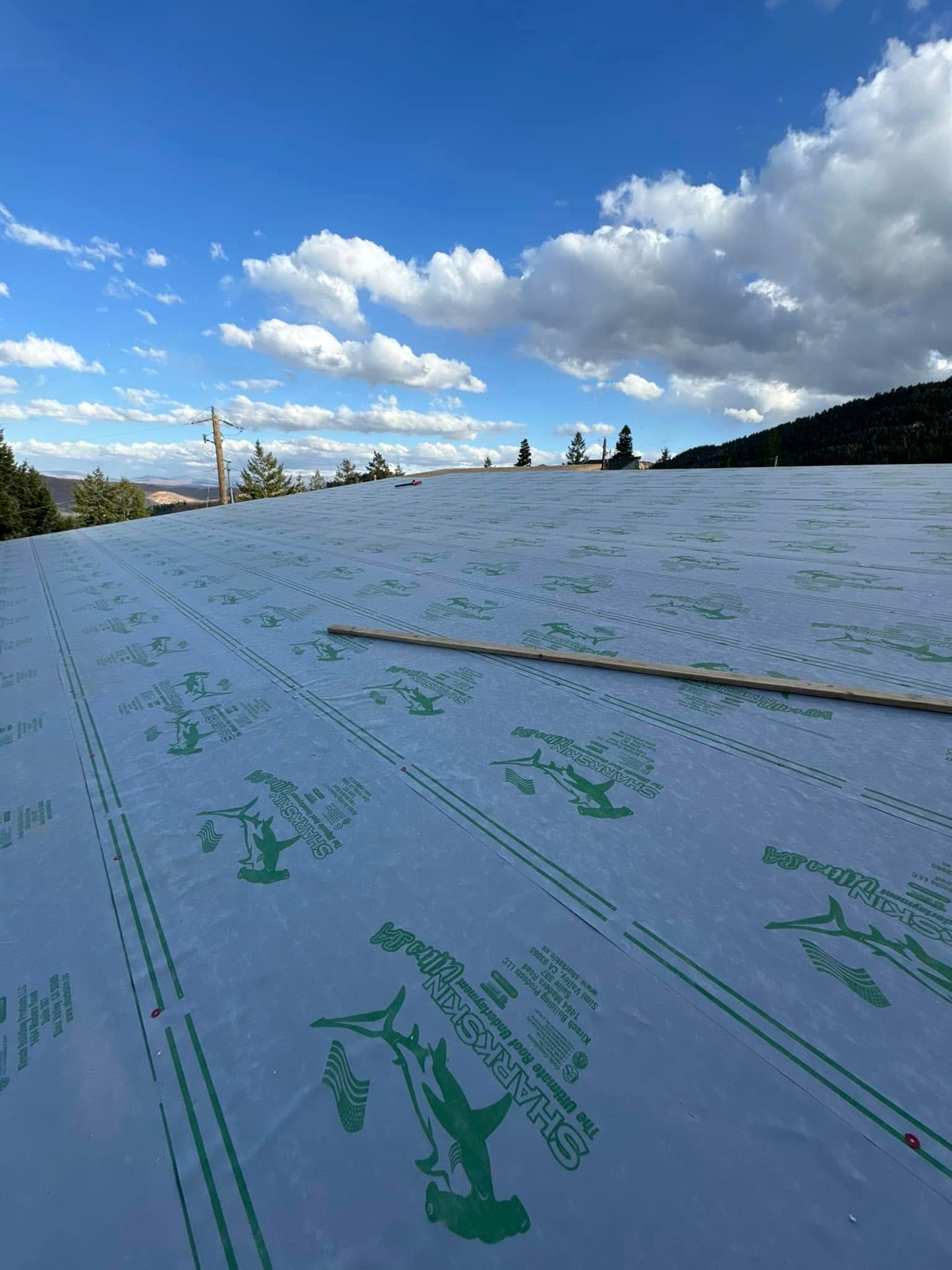 A blue-sky day with puffy clouds over a partially completed roof with patterned green material.