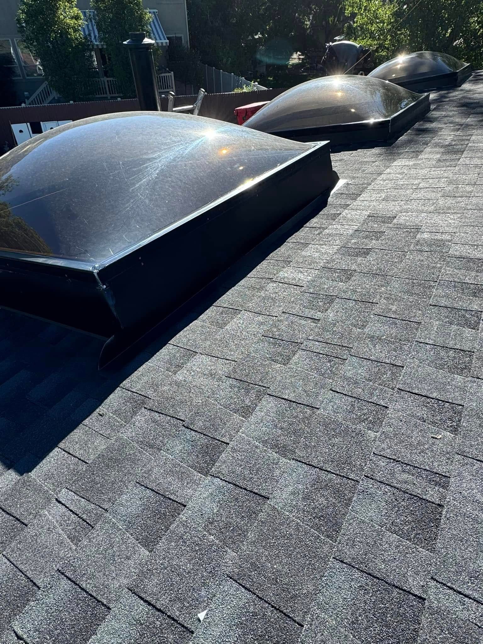 Three dome skylights on a dark gray shingle roof under a bright sky.