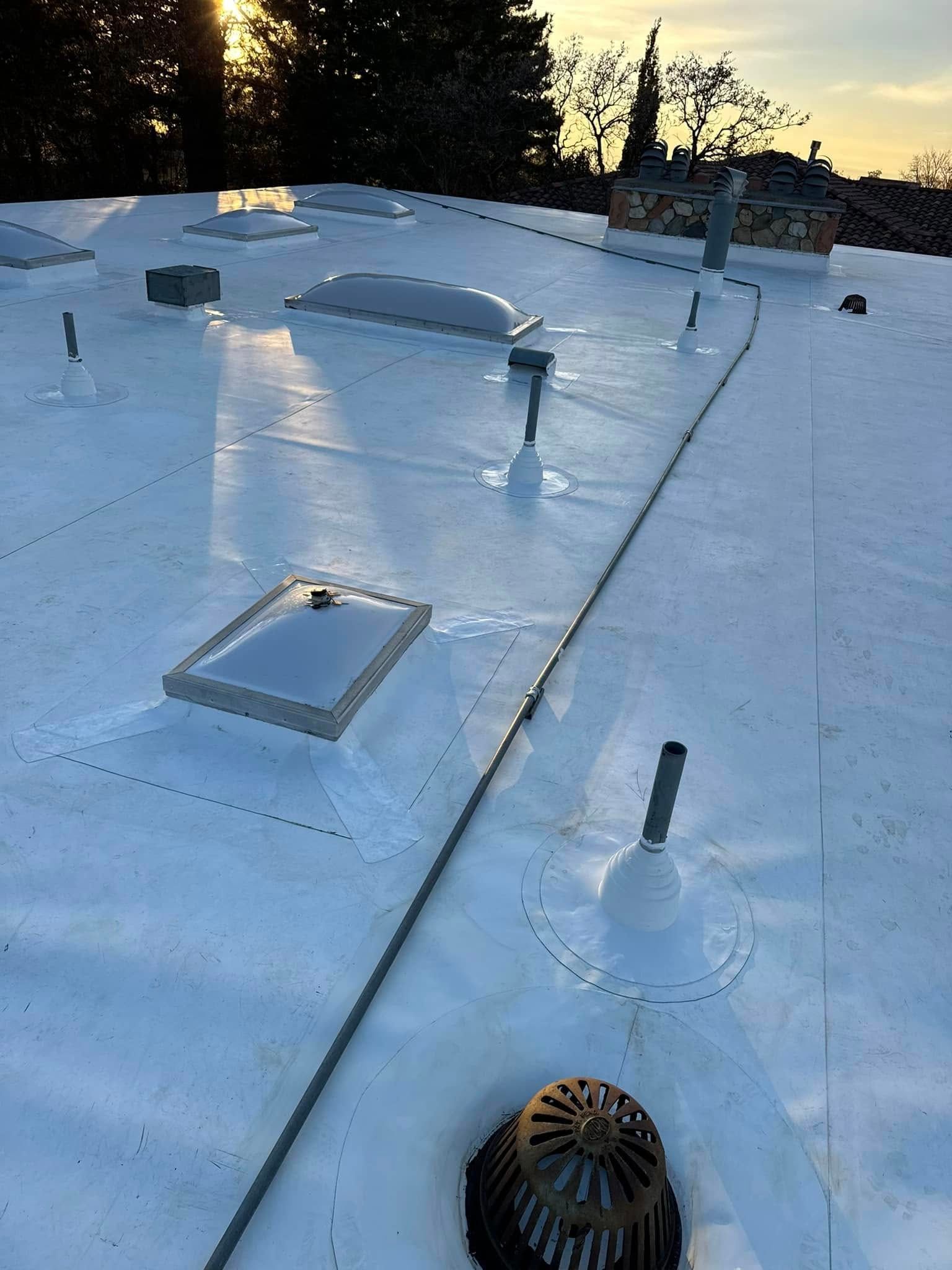 White rooftop with skylights, vents, and drainage; sunset in background.