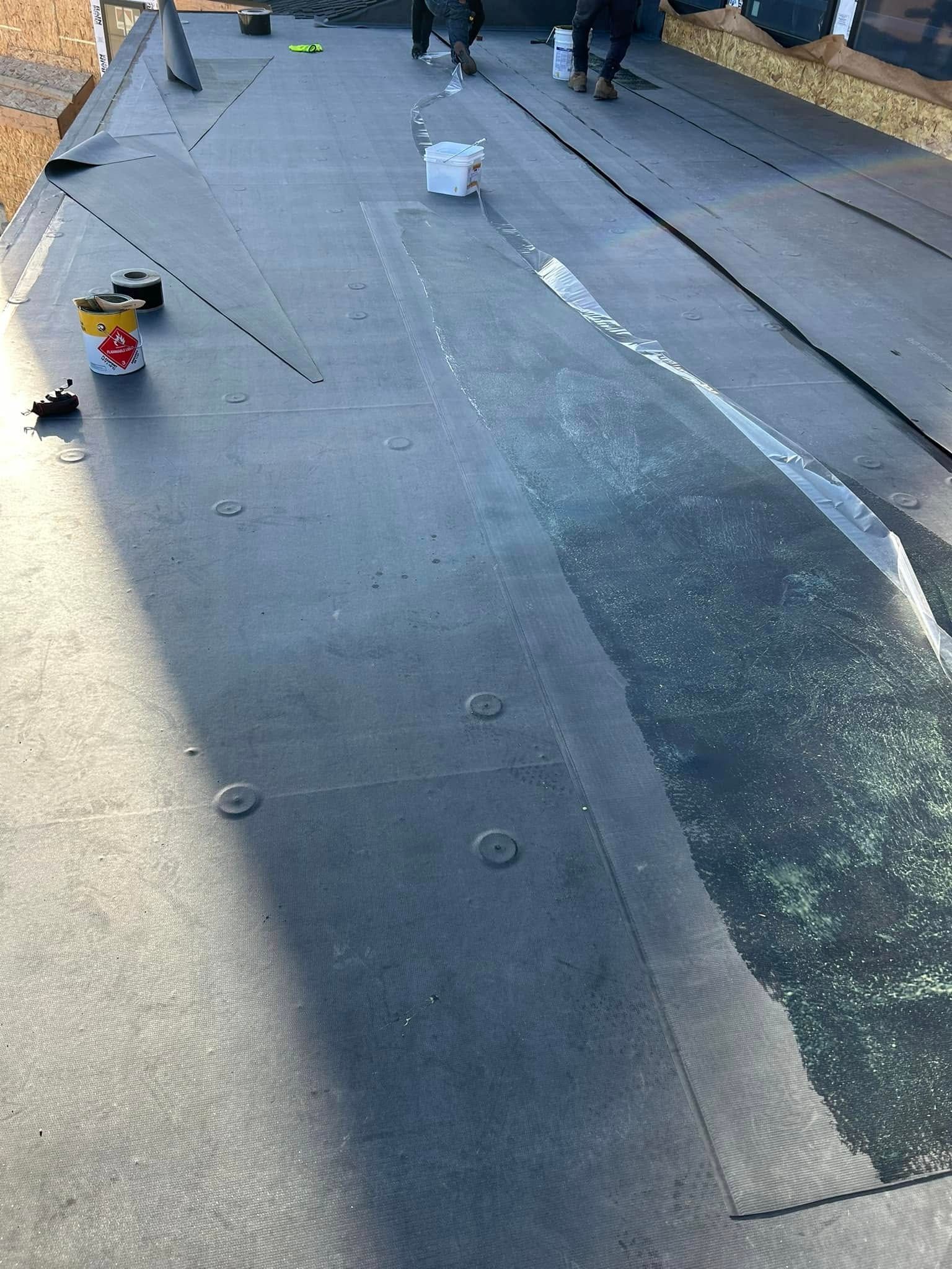 Workers installing roofing material on a rooftop, dark asphalt in process.