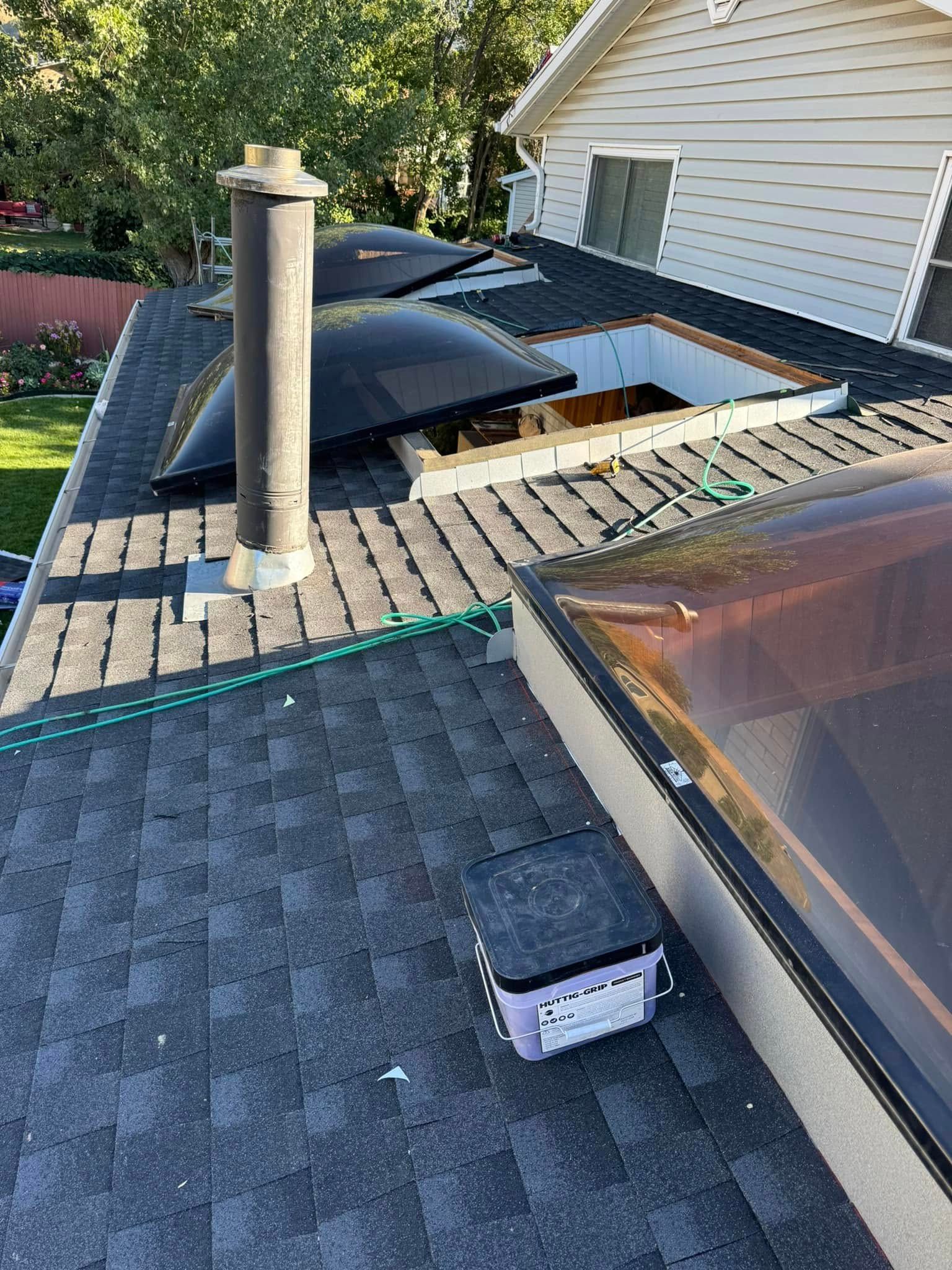 Roof with skylights and a chimney, featuring shingles and a bucket of supplies.