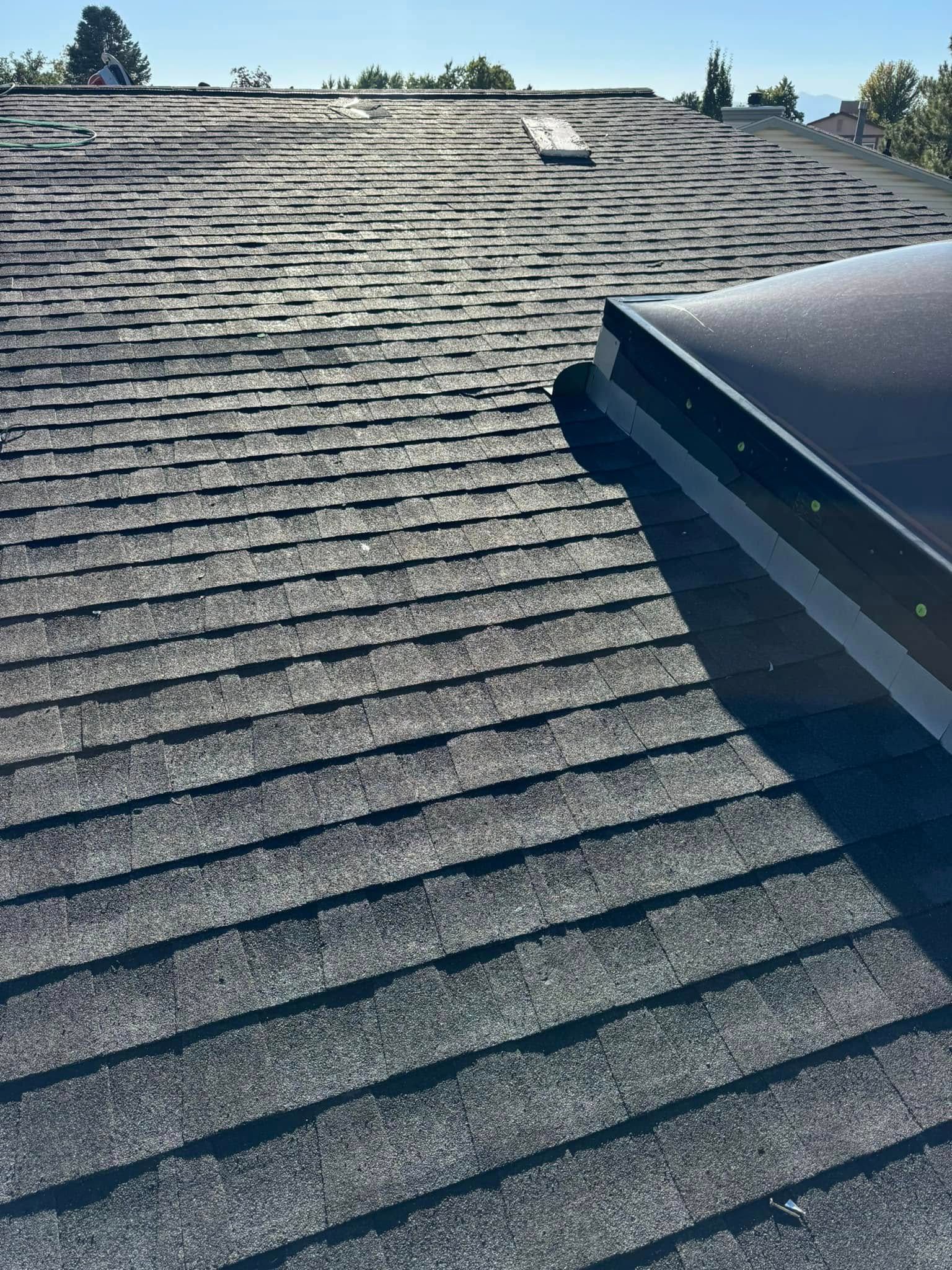Gray asphalt shingle roof with a black skylight. Sunny day.
