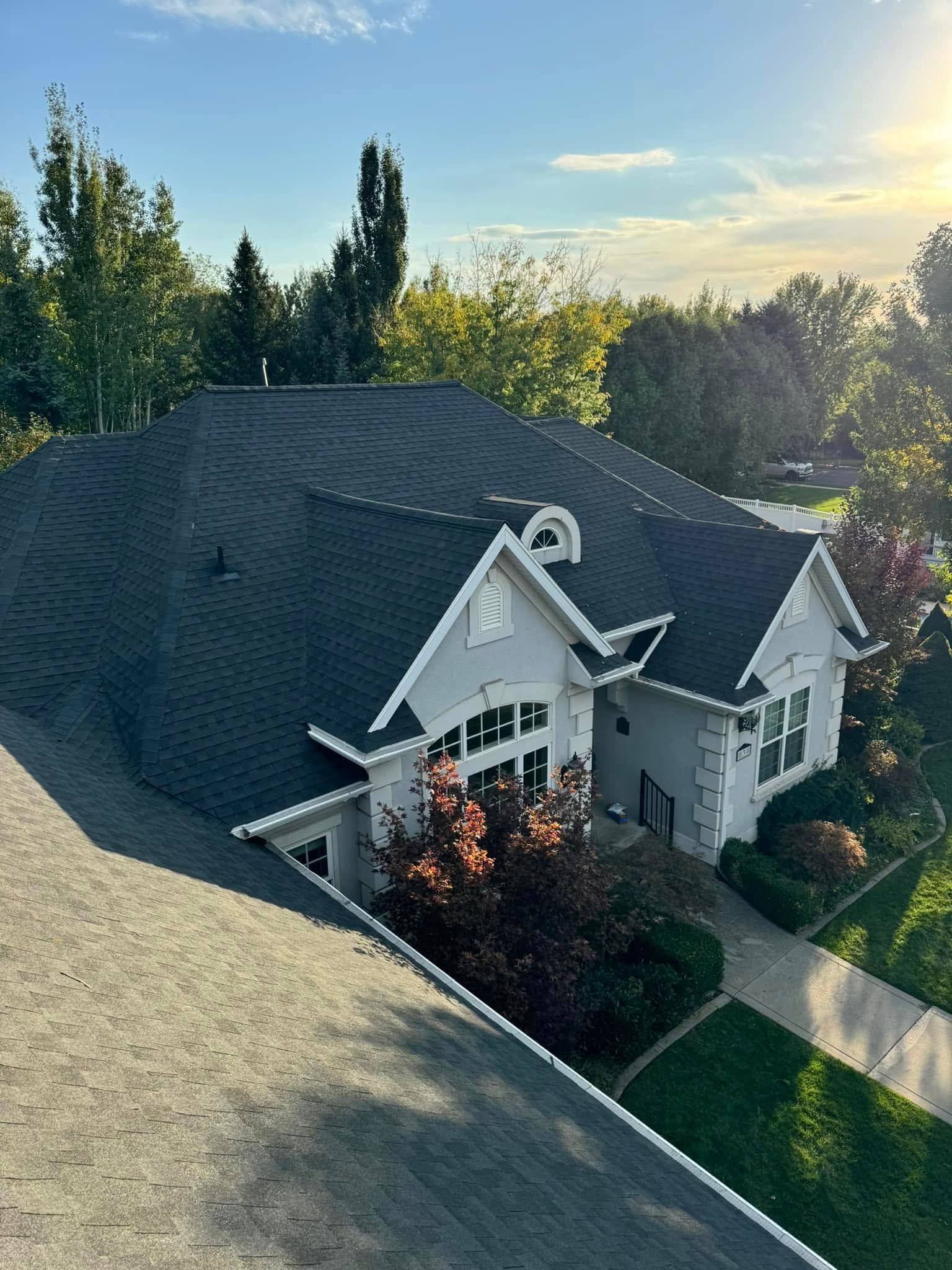 House with dark roof, white trim, and green lawn under a blue sky with trees.