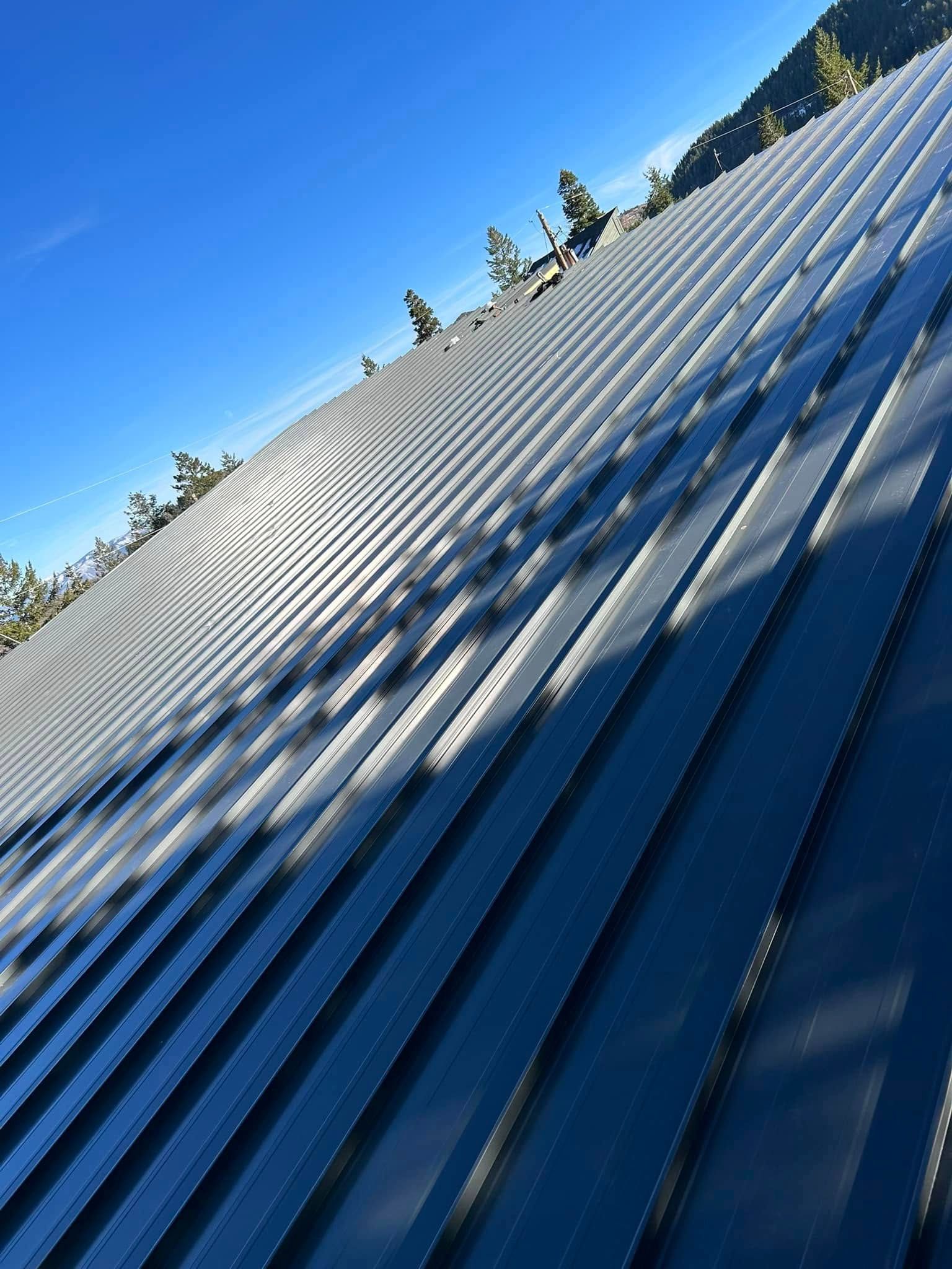 Angled view of a corrugated metal roof with sunlight casting shadows, against a blue sky and mountain landscape.