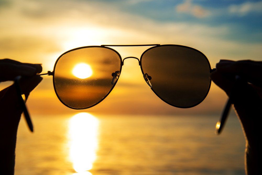 hands holding sunglasses over the ocean