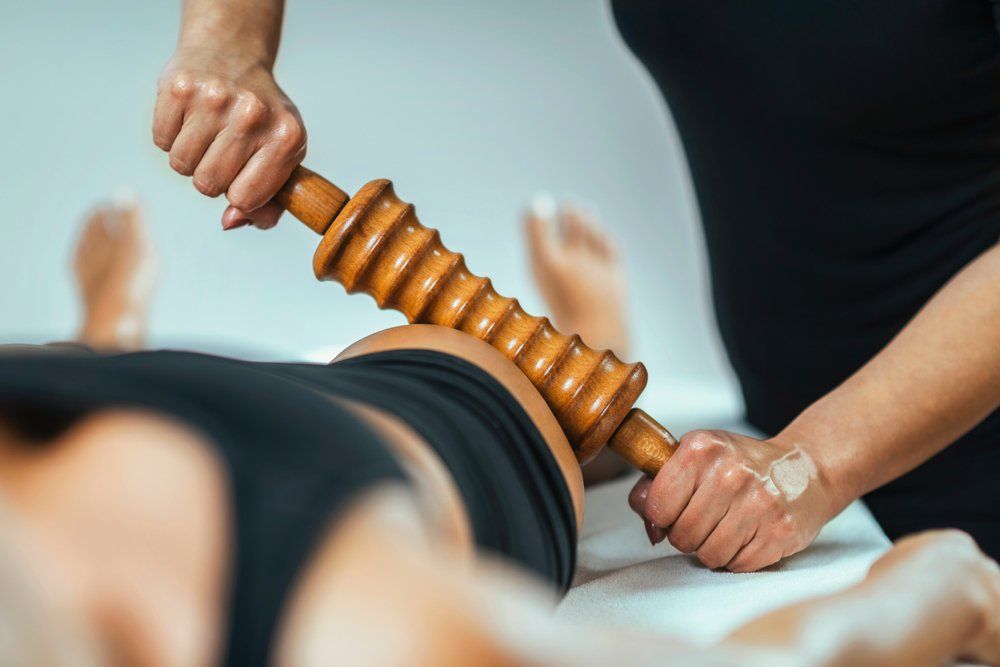 Therapist using a wooden roller tool on a person's hip and thigh during a massage.