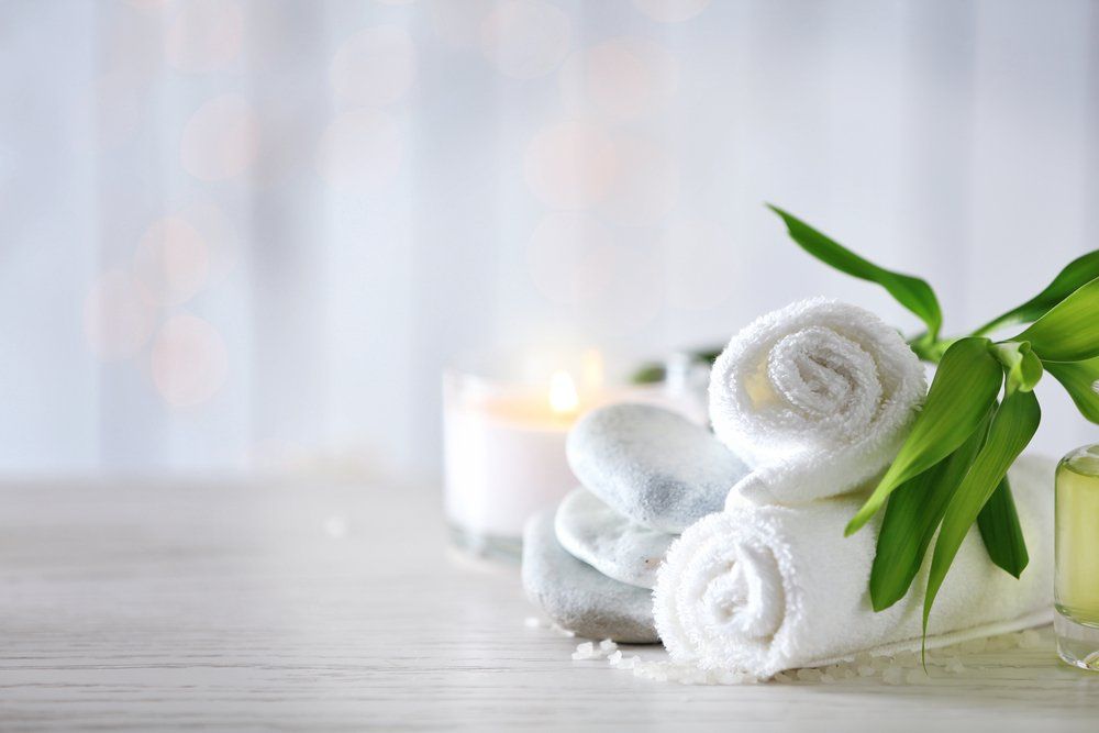 White rolled towels, stones, candle, bamboo, and oil bottle on a wooden surface, soft background.