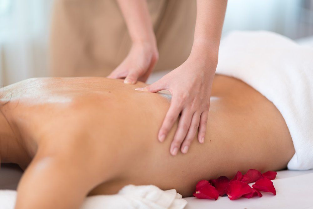 Hands massaging a person's back on a massage table, scattered rose petals, white towel.