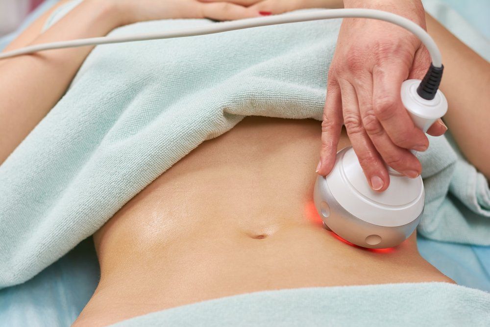 Person receiving abdominal skin treatment with a handheld device, red light visible.