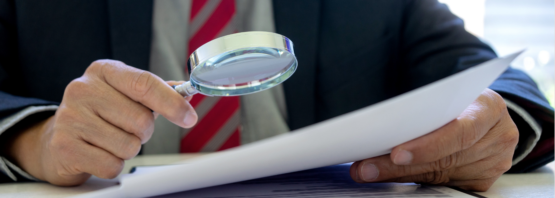 Picture of a person examining a document with a magnifying glass. Picture of a person examining a document with a magnifying glass.
