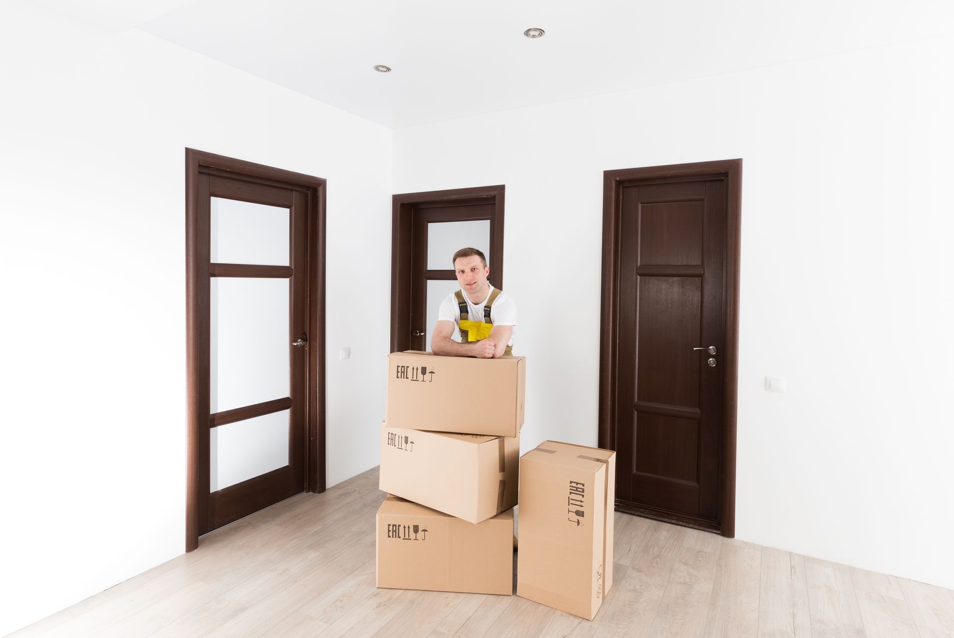 A person in overalls standing near stacked moving boxes in a room with three brown doors.
