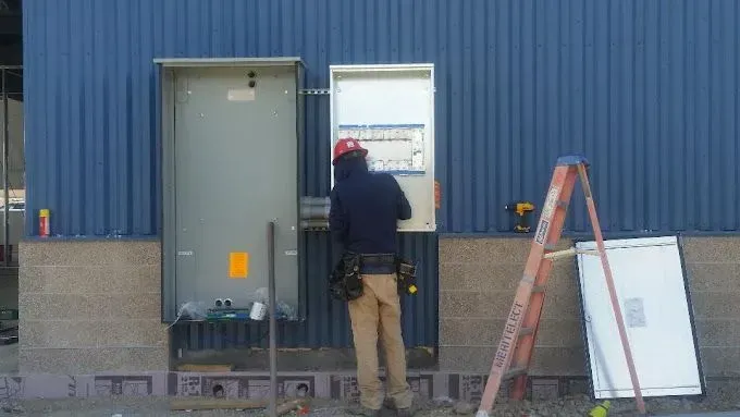 A man is working on an electrical box on the side of a building.