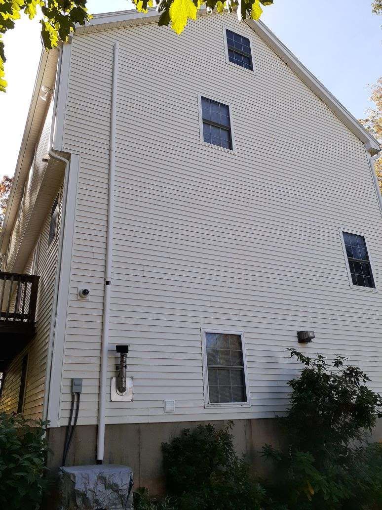 Side view of a white, multi-story vinyl-sided house exterior with several windows and a vertical pipe.