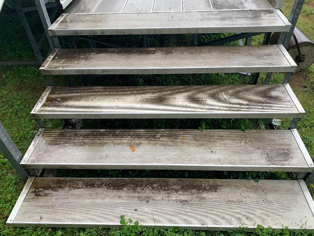 Four outdoor stairs made of faux-wood planks with metal edging, surrounded by grass.