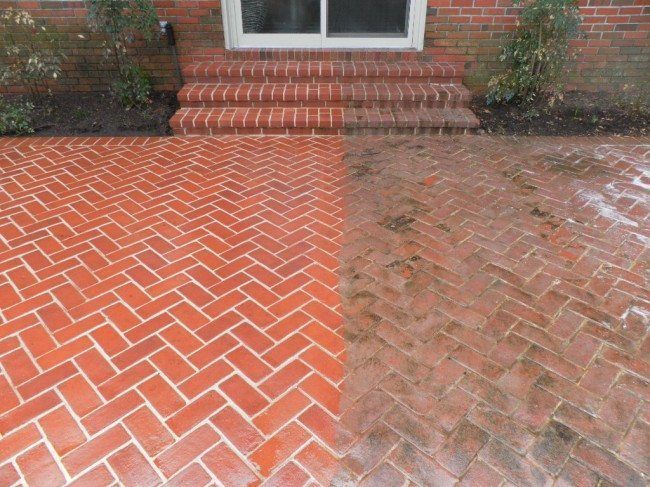 A brick patio partially cleaned by pressure washing, showing a stark contrast between bright, clean bricks and aged, dirty ones.