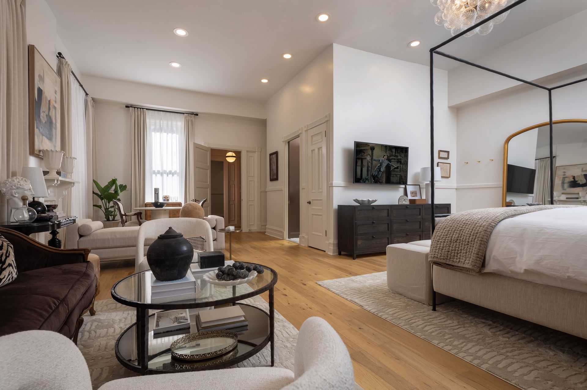 A living room with a canopy bed , couch , chairs , coffee table and television.