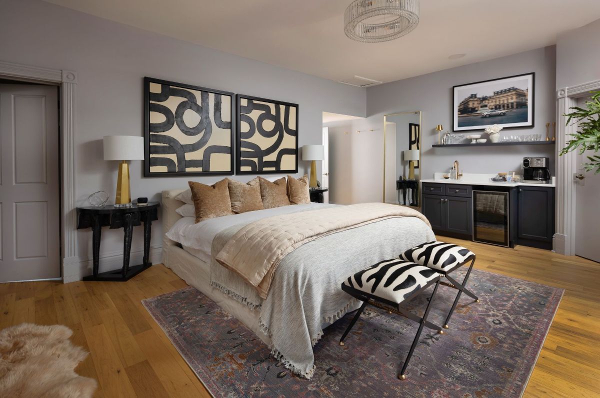 A bedroom with a king size bed , two benches , a rug , and a painting on the wall.