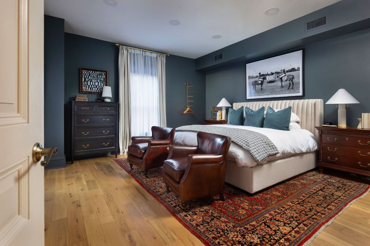 A bedroom with a large bed , chairs , dresser and rug.