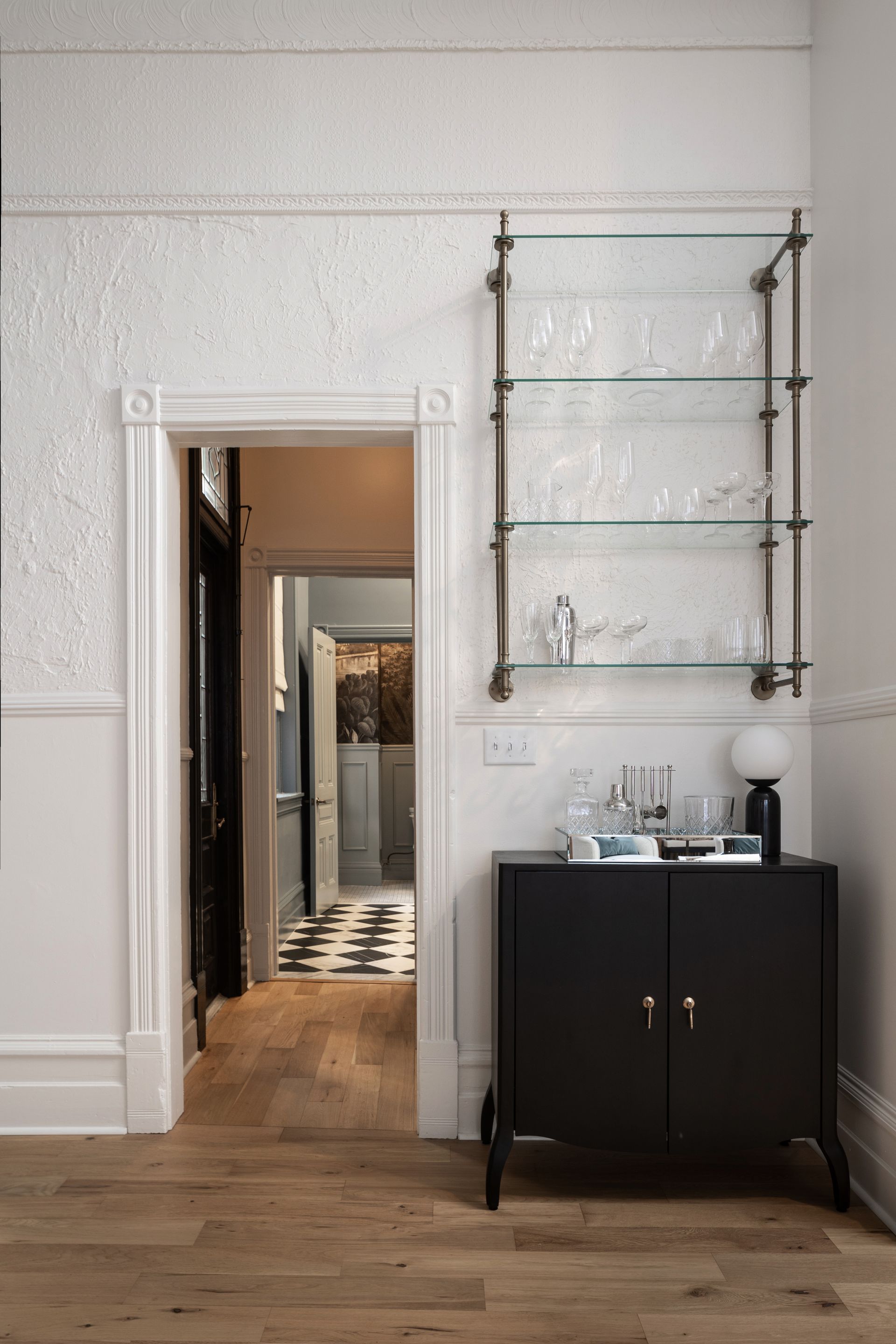 A room with a black cabinet and a glass shelf with glasses on it.