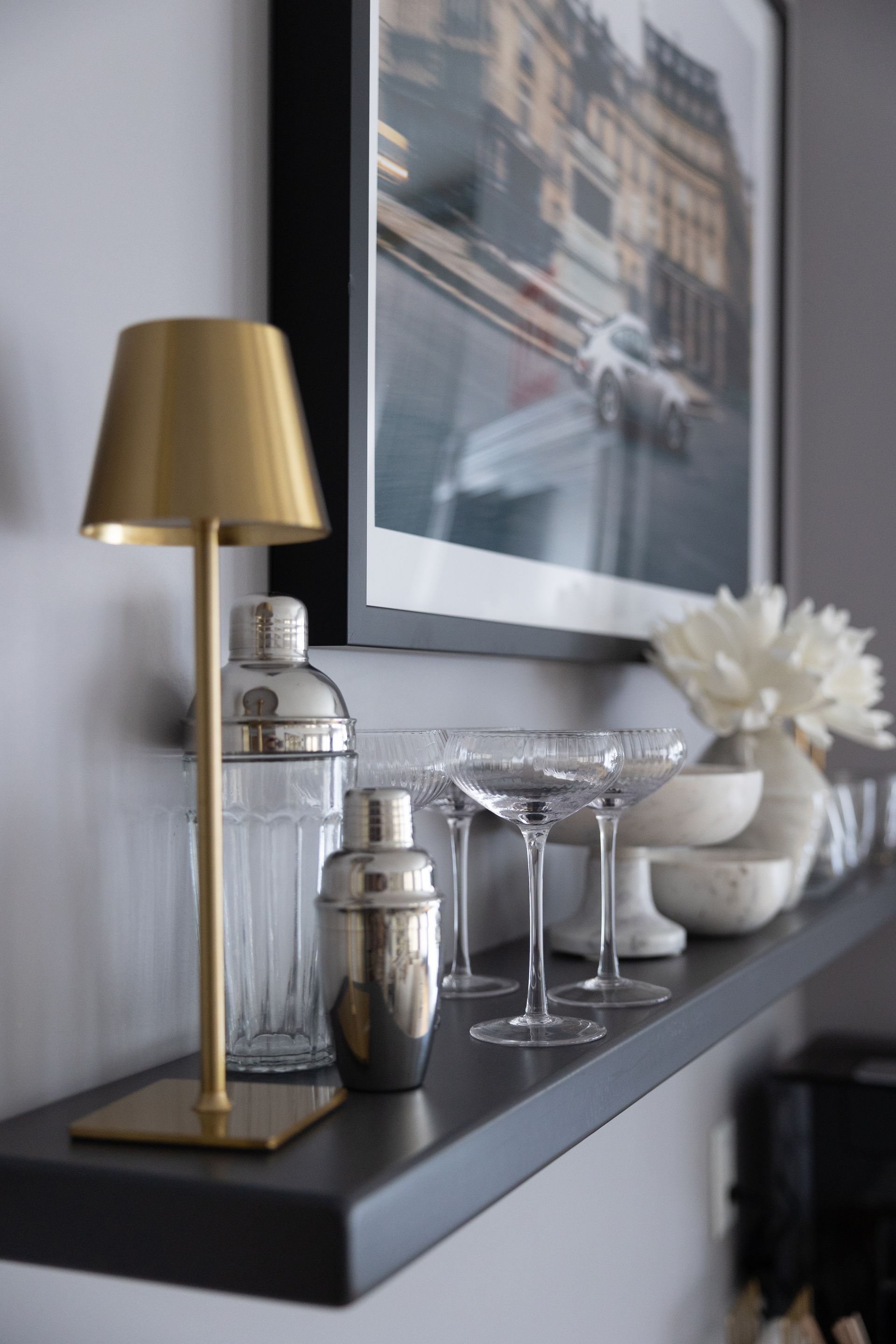 A shelf with a lamp , shaker , glasses and a picture on it.