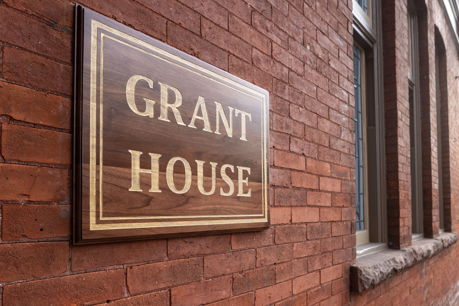 A wooden sign on a brick wall says grant house